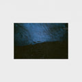 An abstract photographic print depicting a dark, textured blue and black landscape with a small boat silhouette, centered on a light gray background.