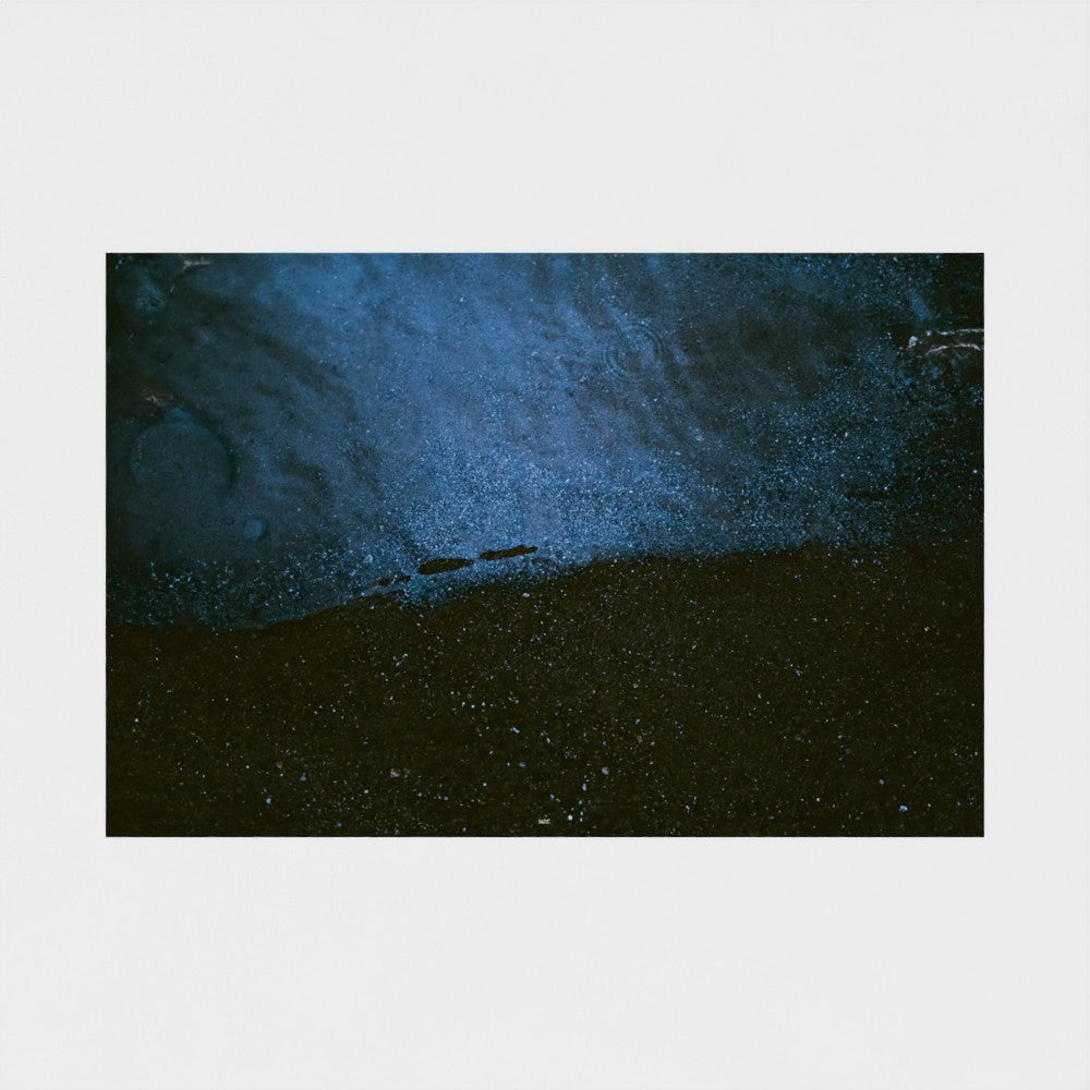 An abstract square art print depicting a dark, textured scene with deep blue and black tones, centered on a light gray background.
