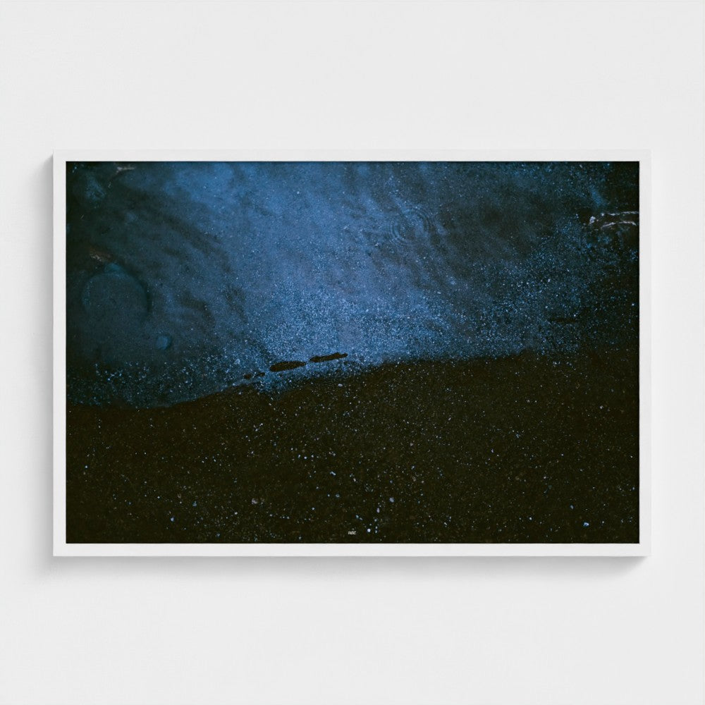 A framed abstract art print featuring a textured, speckled composition of deep blue, navy, and black tones, displayed against a clean white wall.