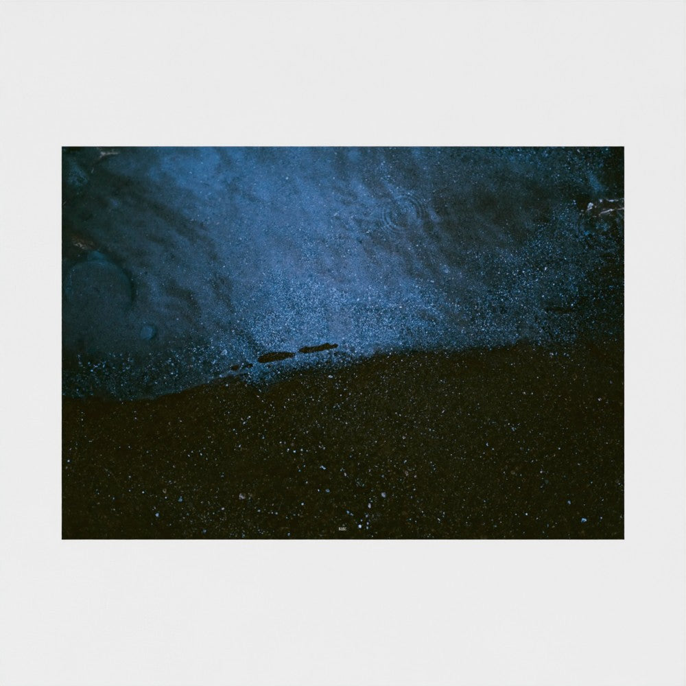 An abstract square art print depicting a textured, dark blue and black landscape with a small boat silhouette, presented on a light gray background.