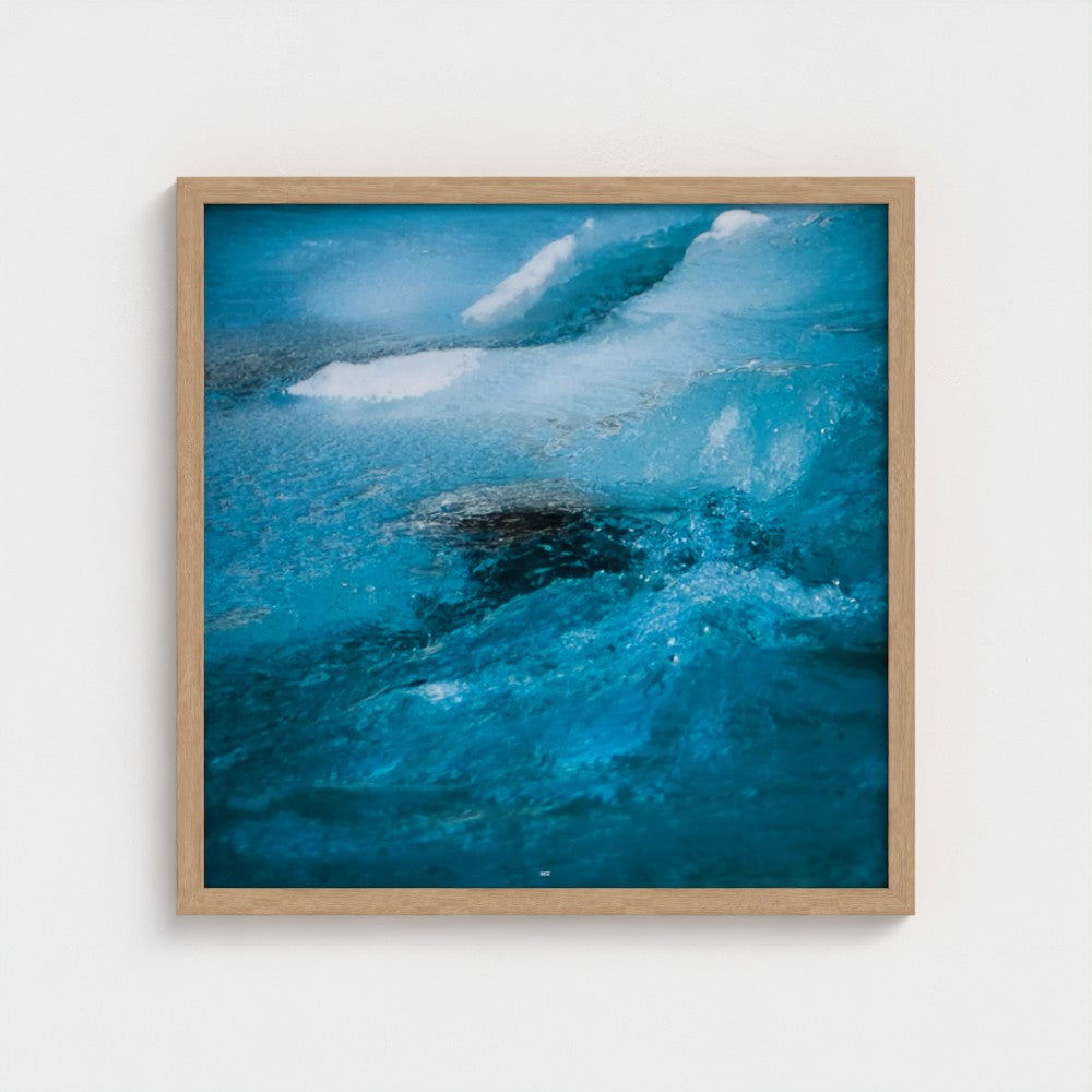A square framed art print depicting a close-up of vibrant blue ocean waves with white foam, set in a light natural wood frame against a clean white wall.