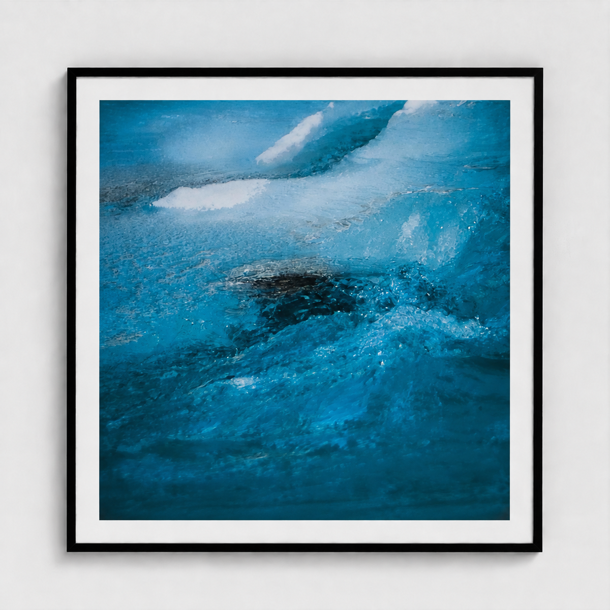 Framed abstract art print depicting a close-up of swirling blue and white water or ice, presented in a black frame with a white mat against a light gray wall.