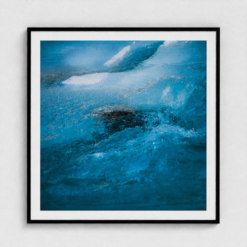 Framed abstract art print depicting a close-up of swirling blue and white water or ice, presented in a black frame with a white mat against a light gray wall.