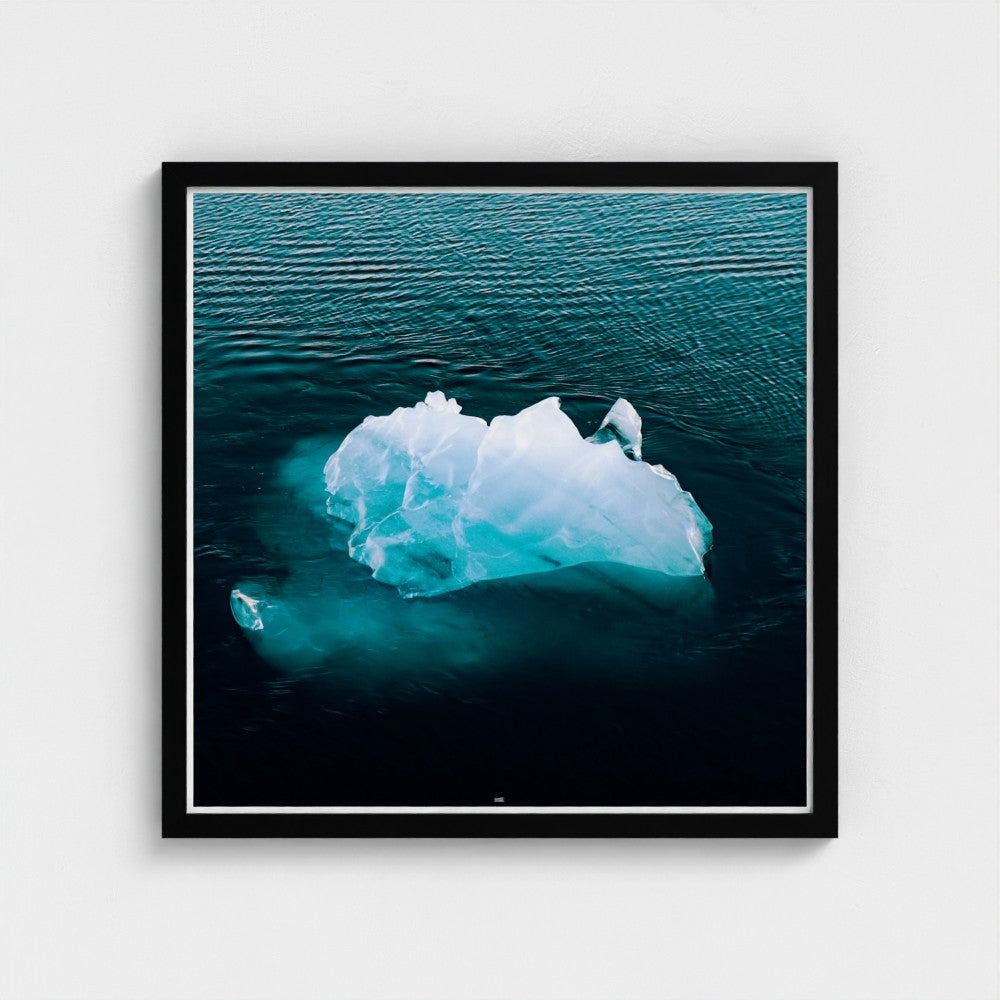 Framed photograph of an iceberg floating in water on a white wall.