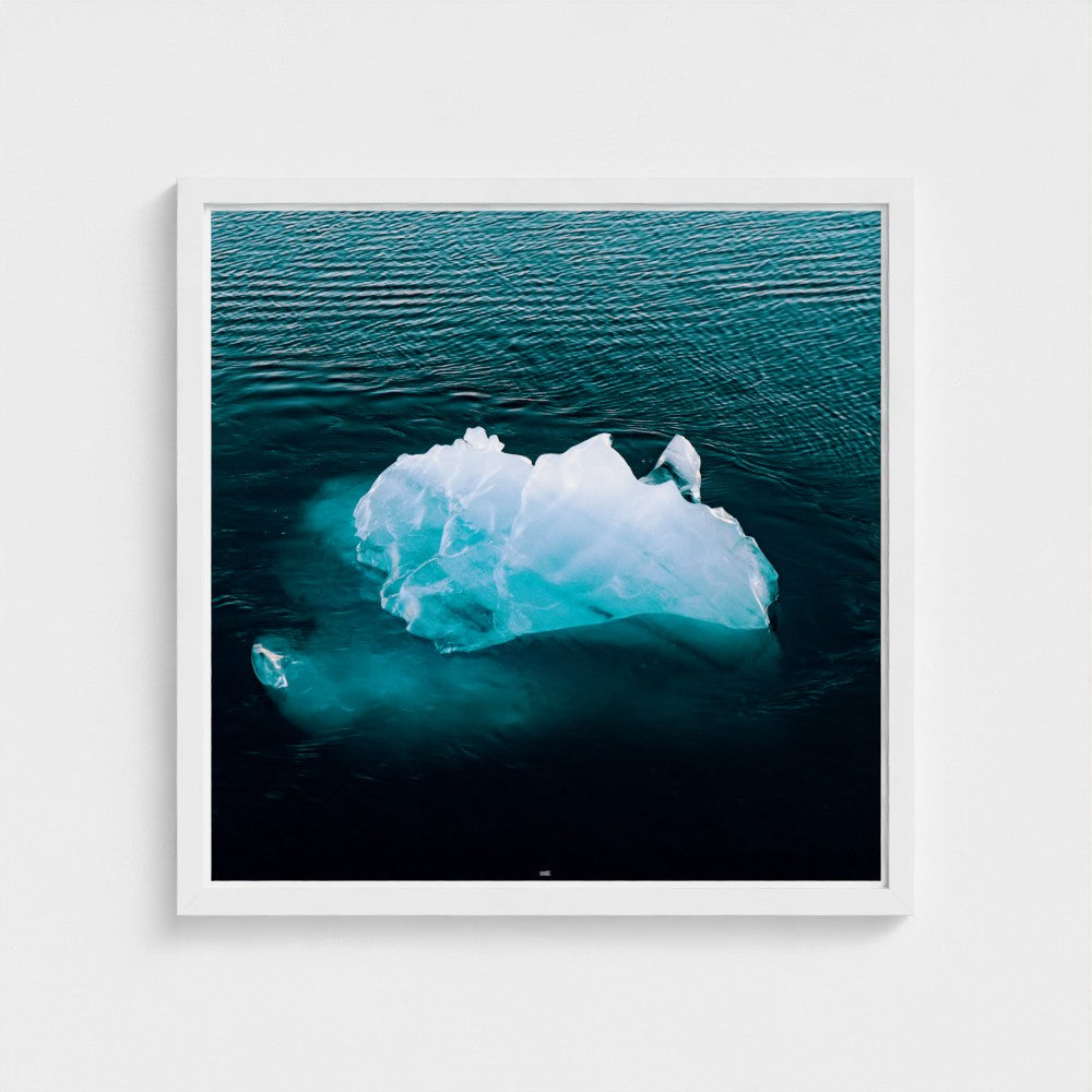Framed photograph of an iceberg floating in water on a white wall.