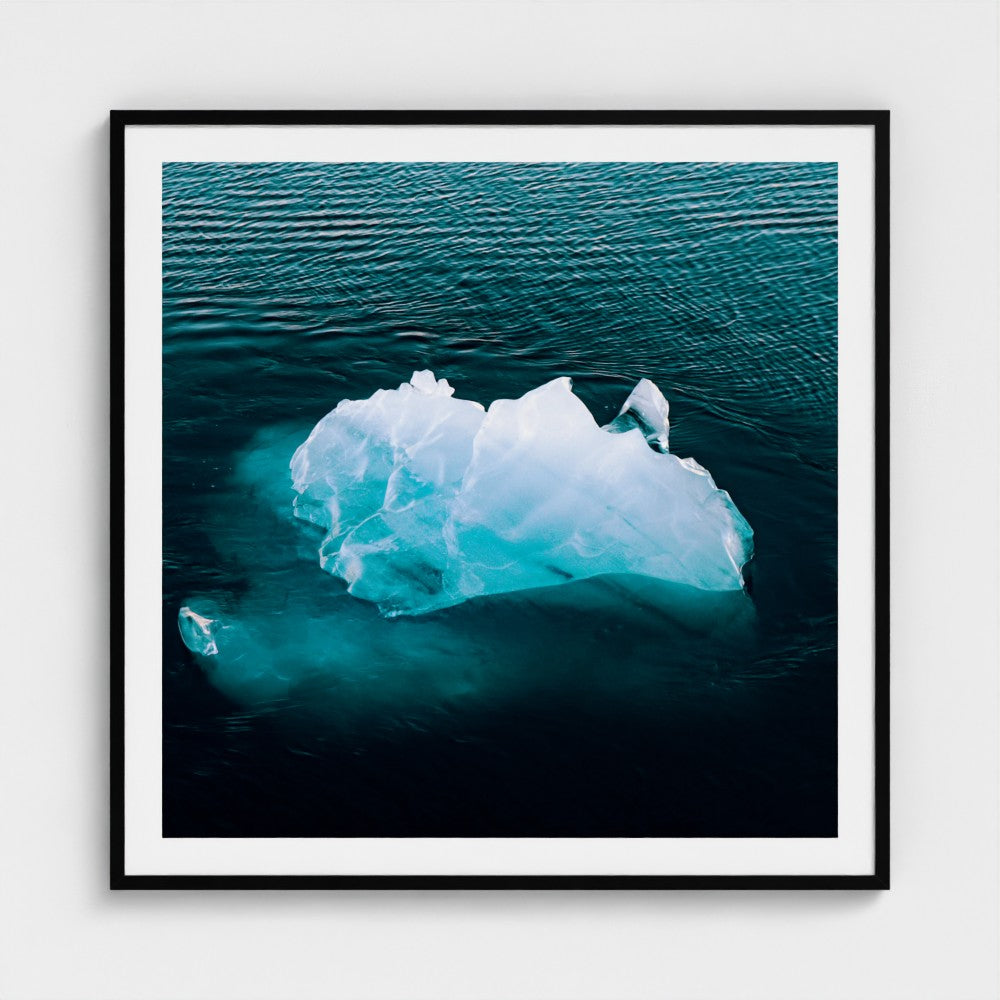 Framed photograph of an iceberg floating in water on a white wall.