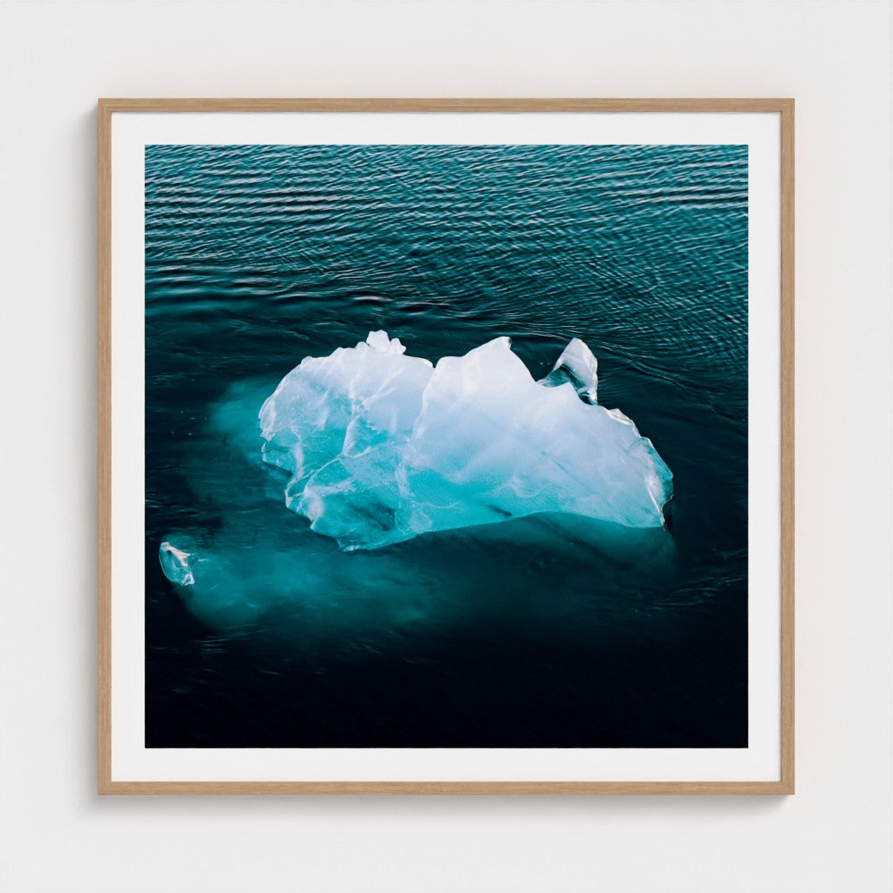 Framed photograph of an iceberg floating in water on a white wall.