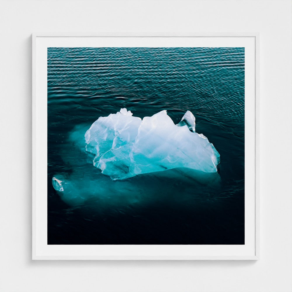 Framed photograph of an iceberg floating in water on a white wall.