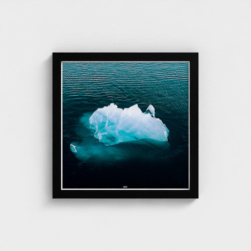 Framed photograph of an iceberg floating in water on a white wall
