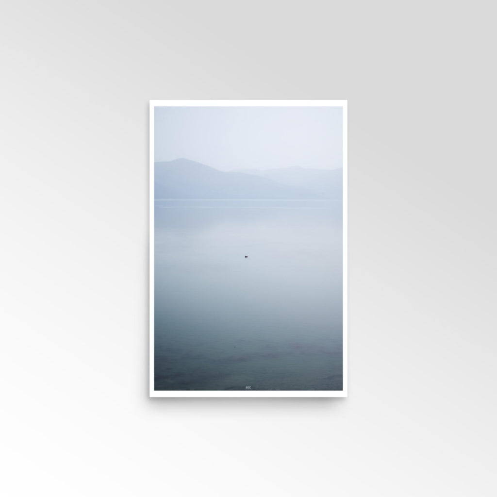 Framed artwork of a landscape with mountains and water on a white wall.