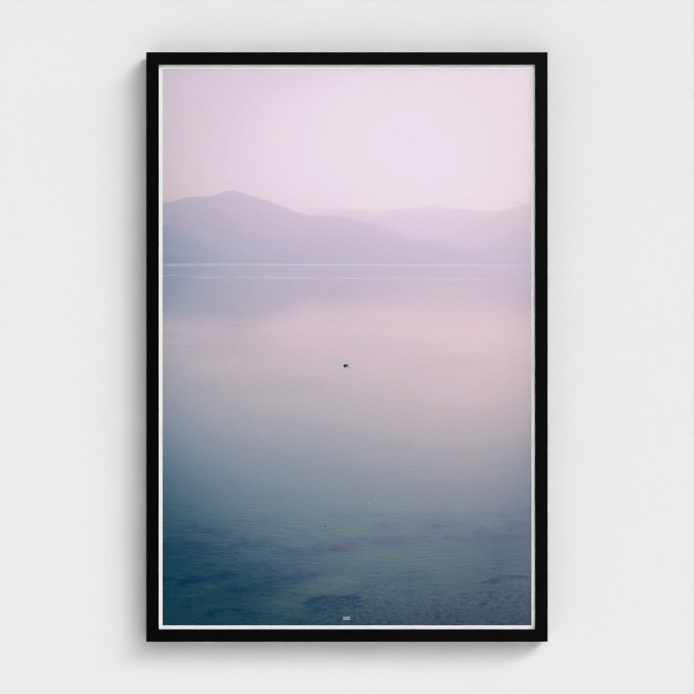 Framed artwork of a landscape with mountains and water on a white wall