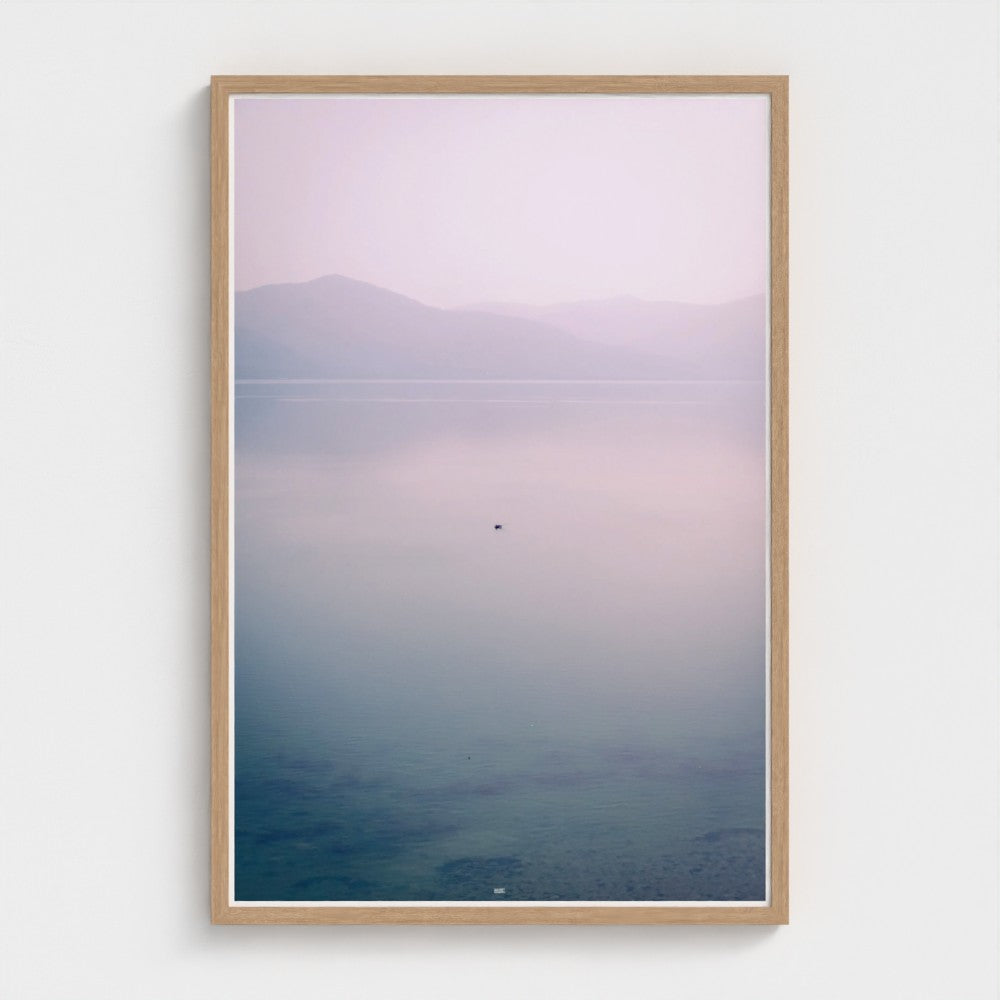 Framed artwork of a landscape with mountains and water on a white wall