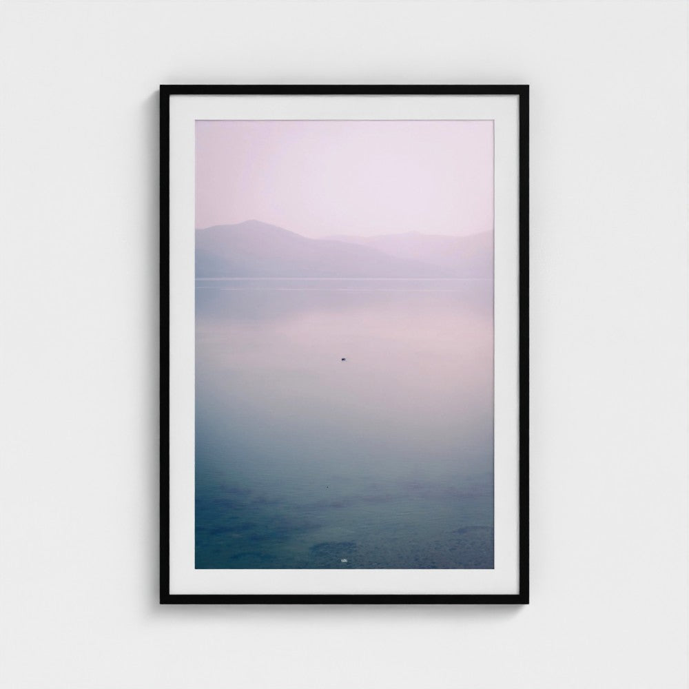 Framed artwork of a landscape with a mountain and water on a white wall