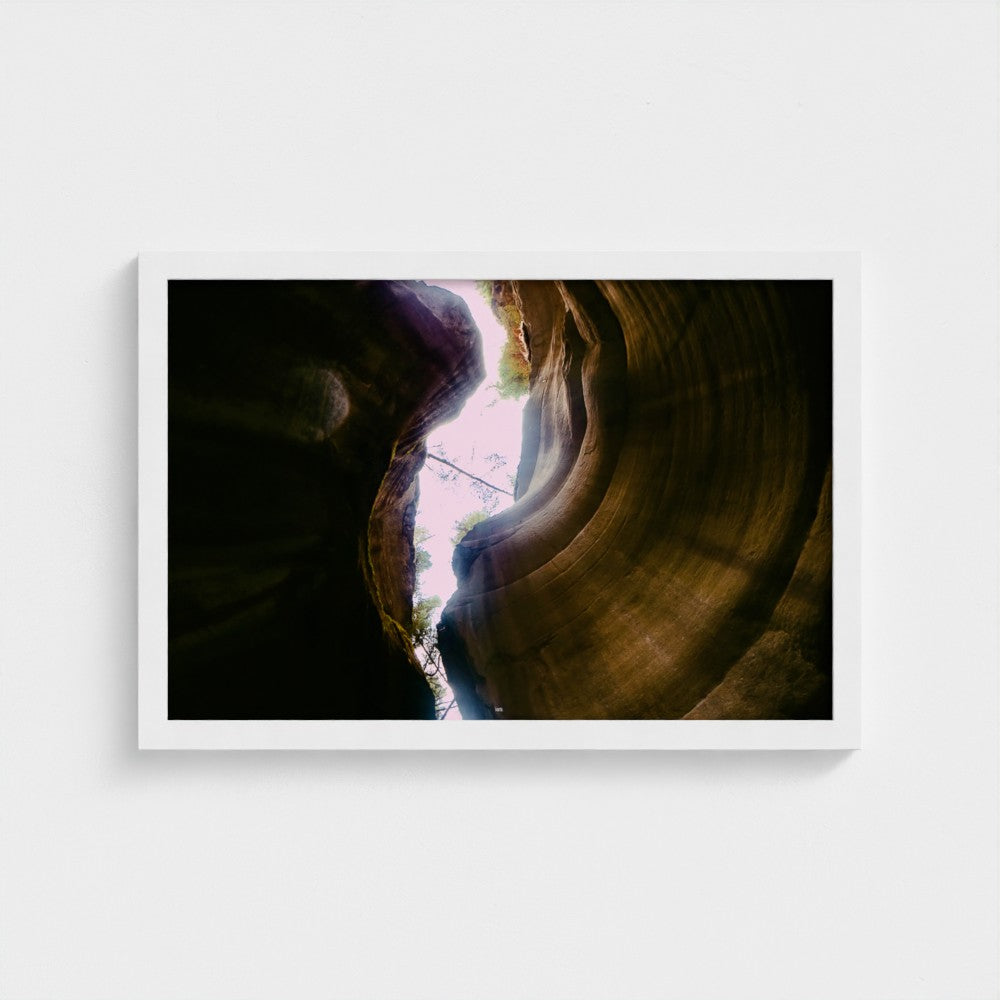 A framed photographic print of a slot canyon interior with light streaming in from above, displayed against a clean white wall.