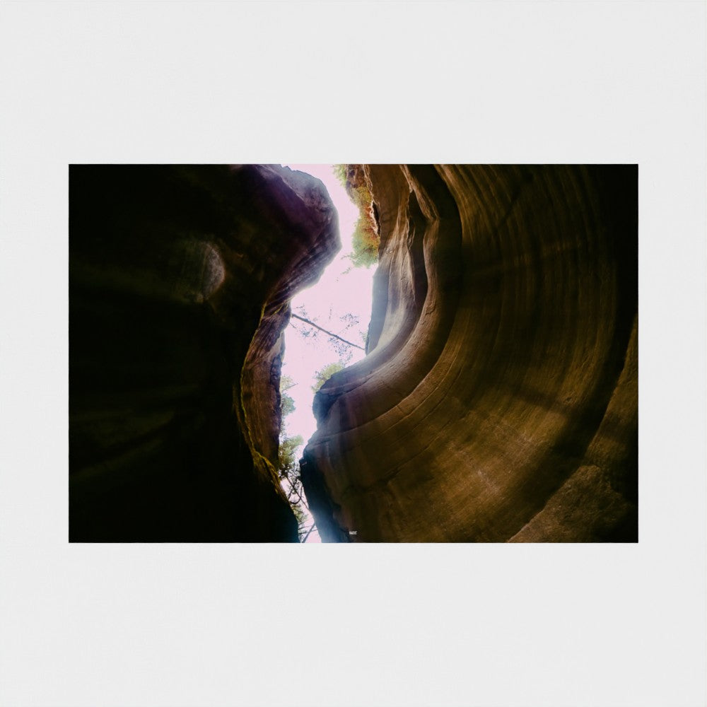 A rectangular photographic print showing a dramatic slot canyon with curved rock walls and light beams, centered on a light gray background.