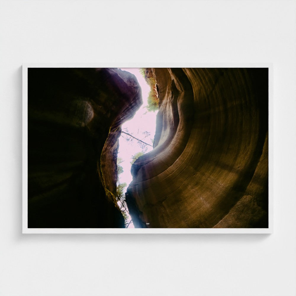 A framed photographic print of a slot canyon with dramatic light rays shining through the rock formation, displayed on a clean white wall.
