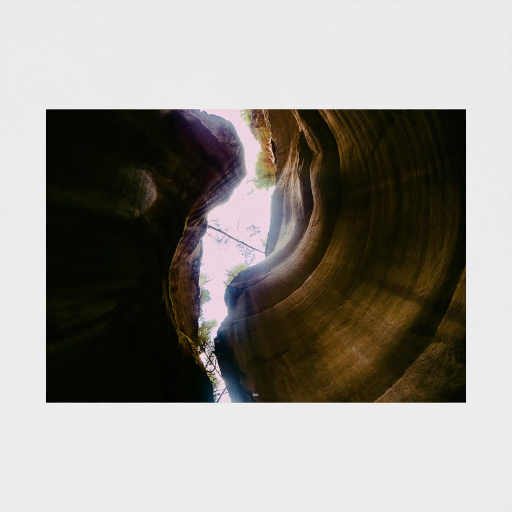 A landscape photograph of a slot canyon looking up at the curved sandstone walls, with light filtering from the canyon opening above, presented as a square art print on a light gray background.