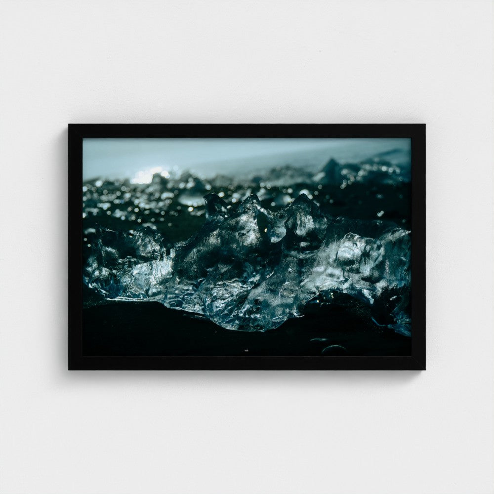 A framed photographic print of dark, textured ice or glass-like formations in deep blue and black tones, presented in a black frame against a light gray wall.
