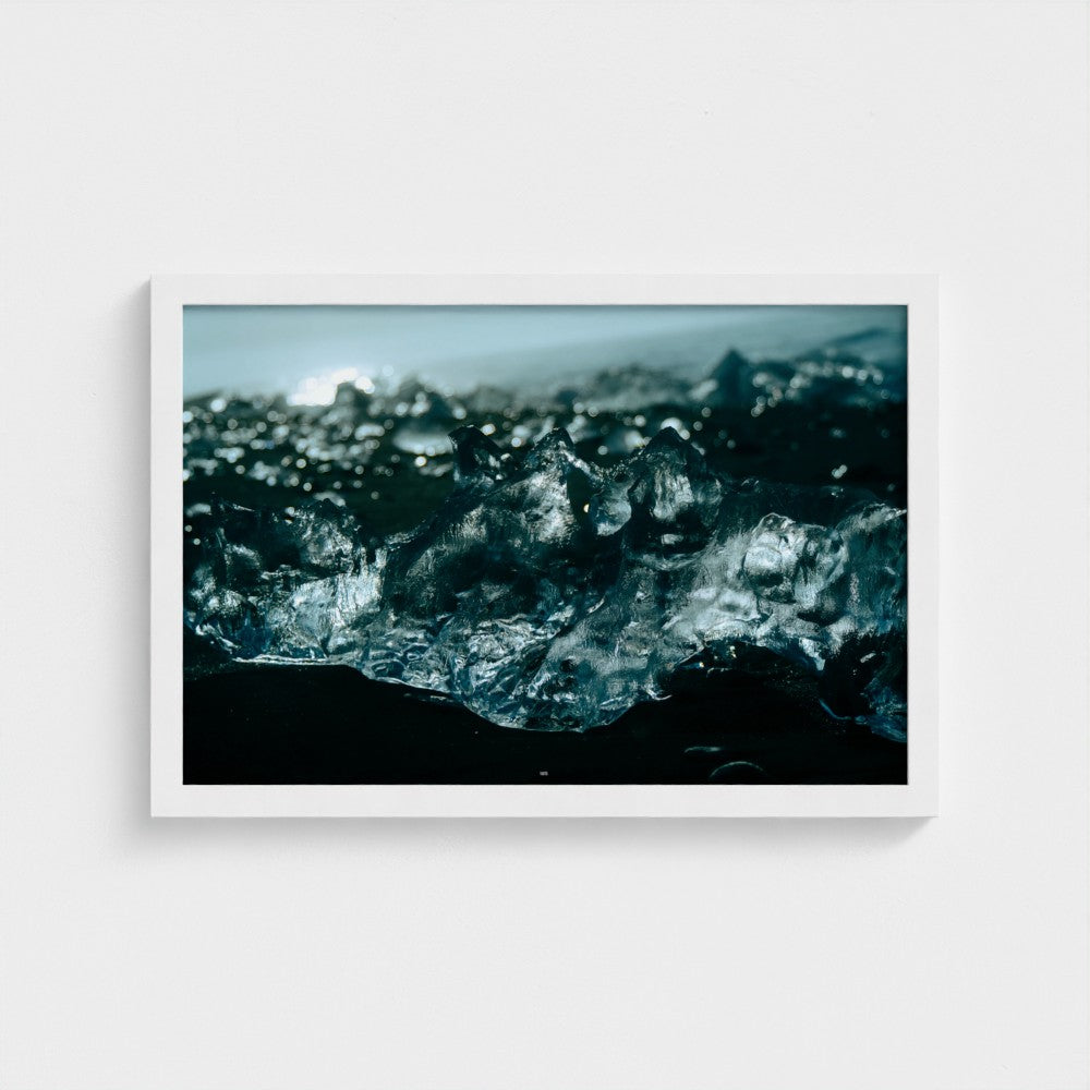 A framed photographic art print of black sand beach ice blocks in Iceland, featuring a white frame against a light gray wall.