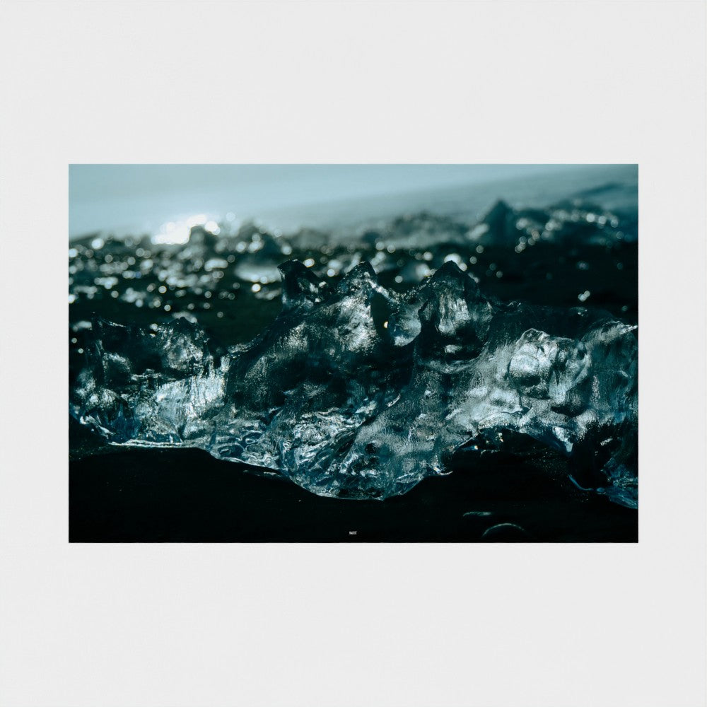 A square photographic print of dark, textured ice or glass-like formations in deep blue and black tones, centered on a light gray background.