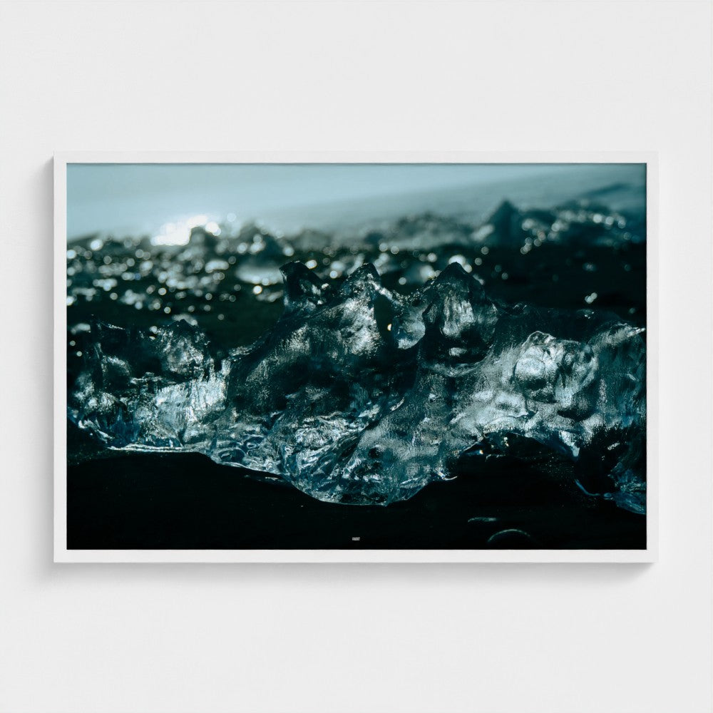 A framed photographic print of dark blue-black ice formations on a black sand beach, displayed against a clean white wall.