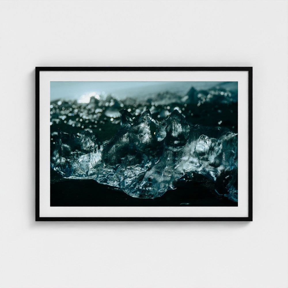 A framed photographic print of a close-up ice and water scene in deep blue and black tones, displayed on a light gray wall.