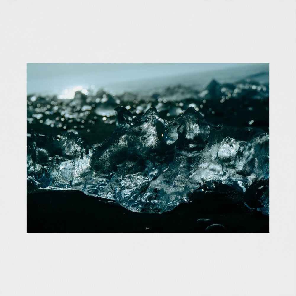 A square photographic art print depicting a close-up of translucent ice cubes on a dark shore, presented with a wide white border on a light gray background.