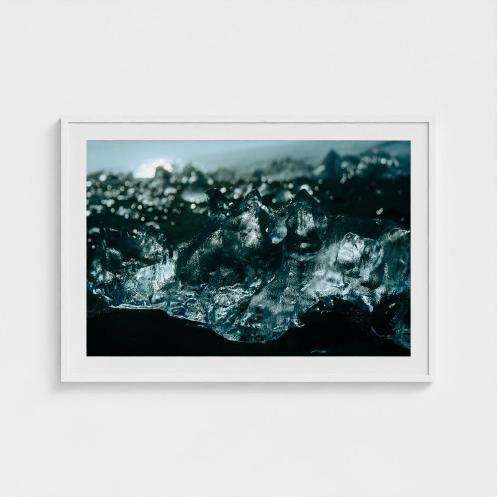 A framed photographic print of a dark, moody close-up landscape with icy, crystalline forms in deep blue, teal, and black tones, displayed against a light gray wall.