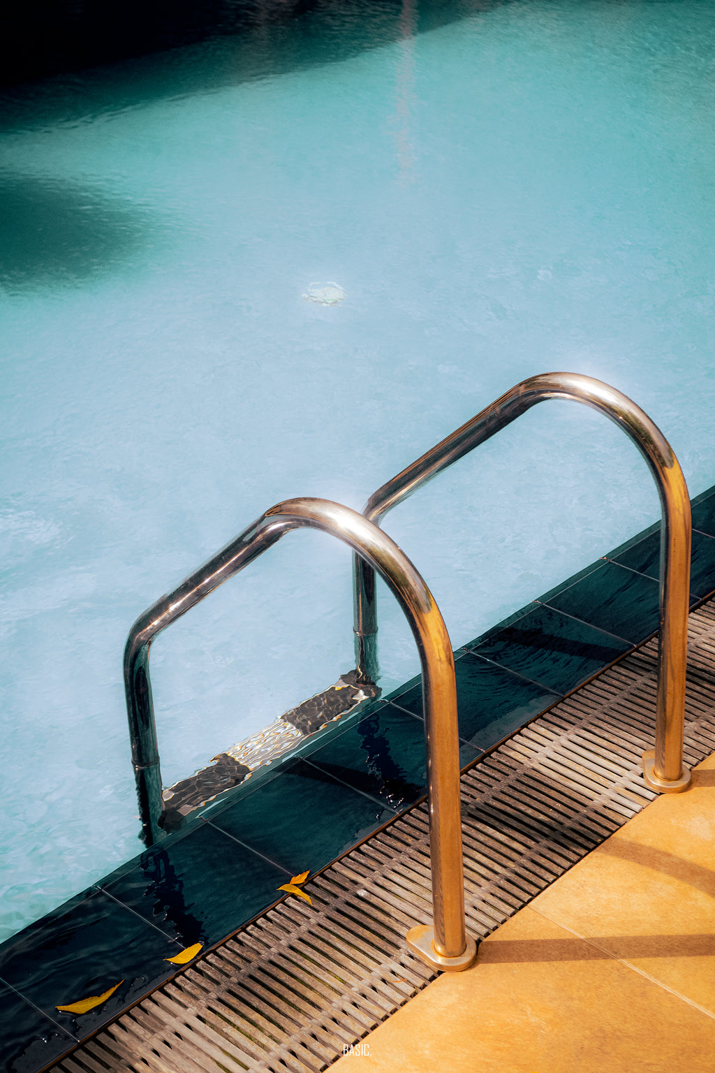 Metal ladder on a pool deck with clear blue water