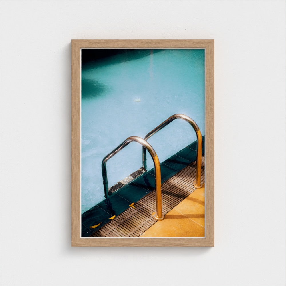 Framed photograph of a pool with a metal ladder on a white wall