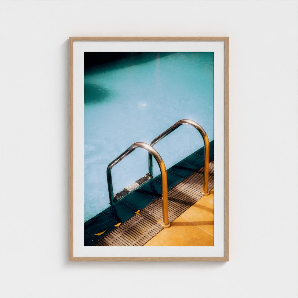 Framed photograph of a pool with a metal ladder on a white wall
