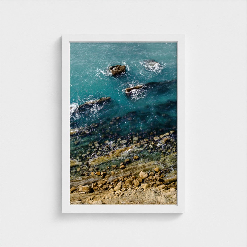 Framed artwork of a coastal scene with rocks and water.