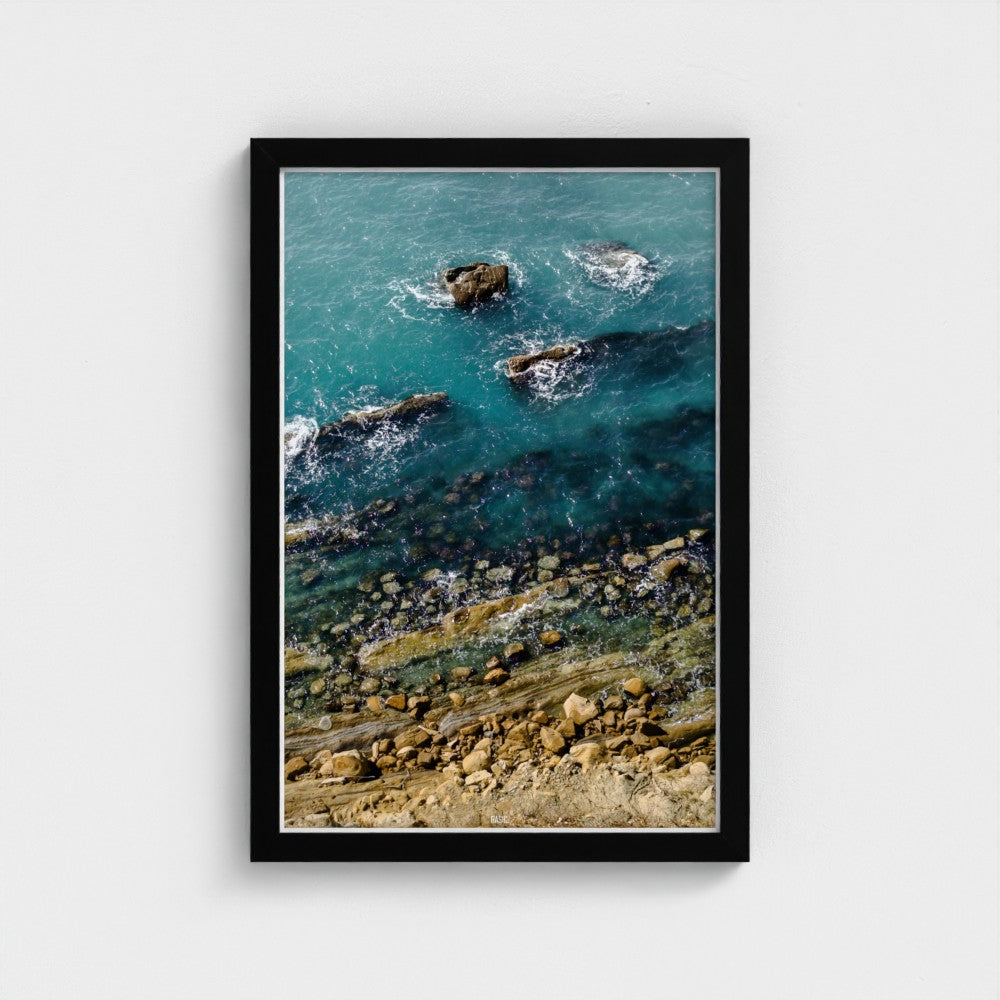 Framed artwork of a coastal scene with rocks and water.