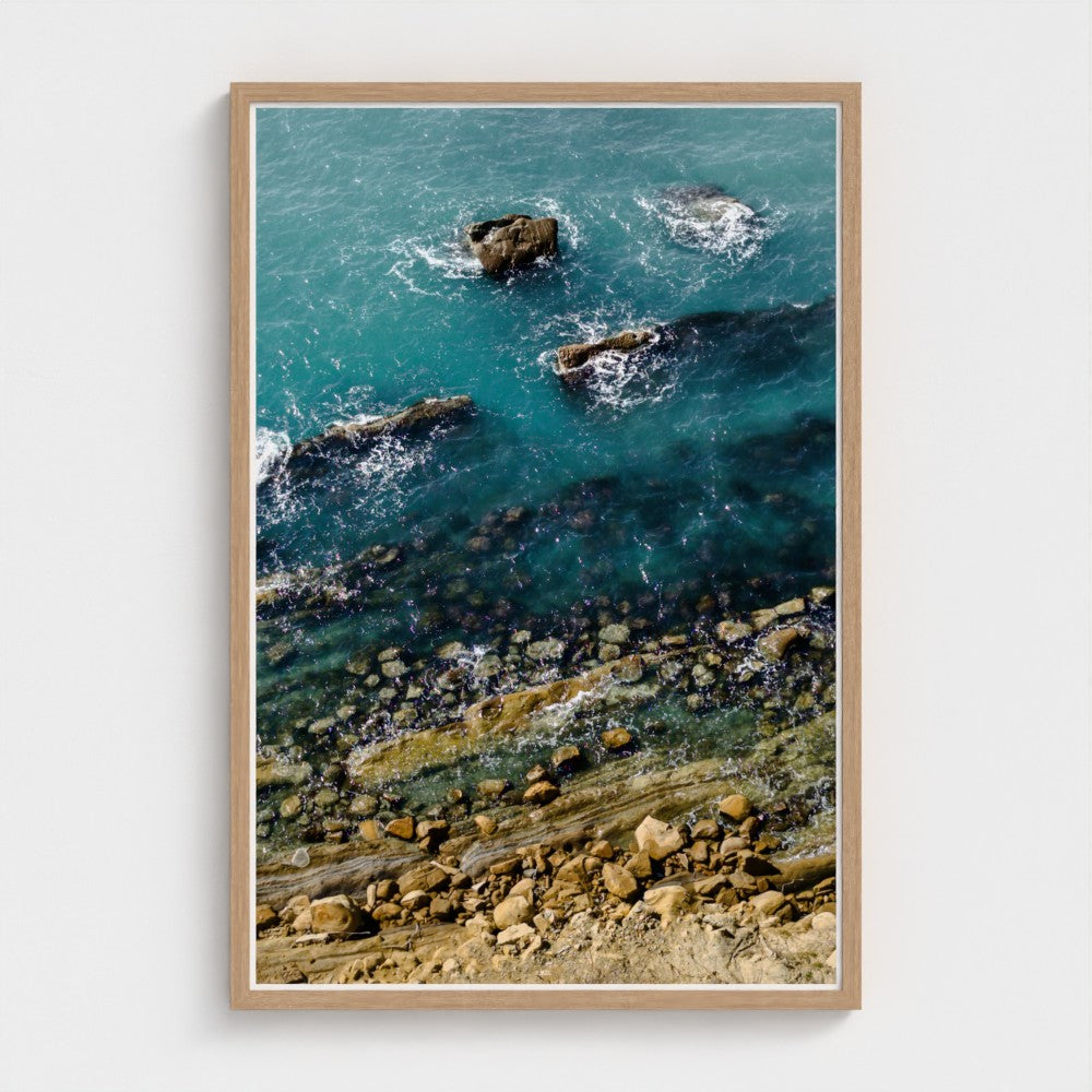 Framed artwork of a coastal scene with rocks and water.