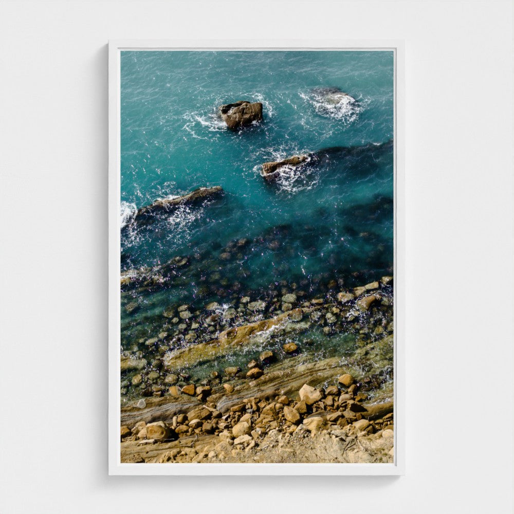 Framed artwork of a coastal scene with rocks and water.