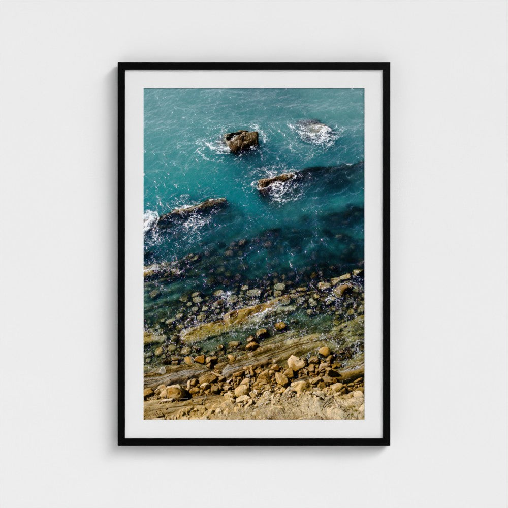 Framed artwork of a coastal scene with rocks and water.