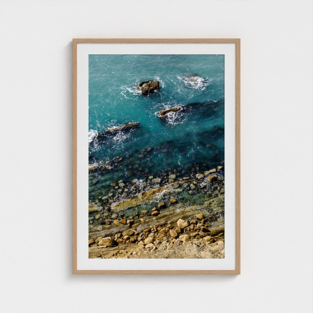 Framed artwork of a coastal scene with rocks and water.