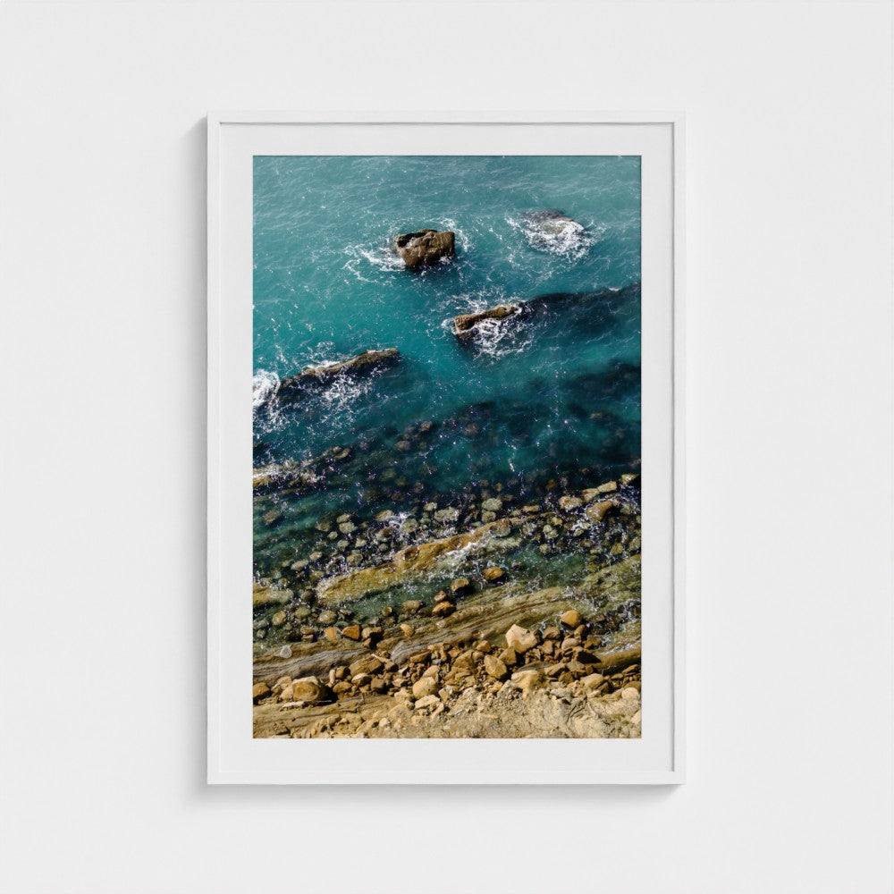 Framed artwork of a coastal scene with rocks and water.