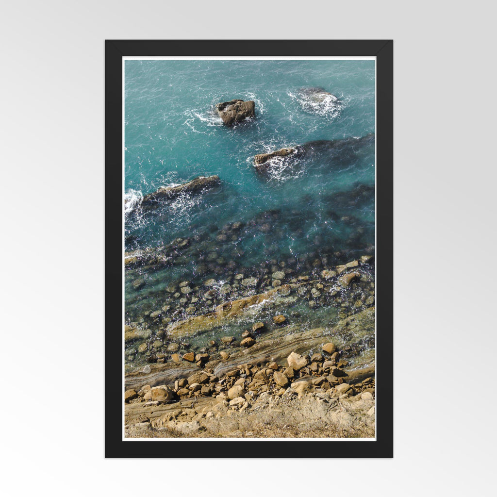 Framed artwork of a coastal scene with rocks and water.