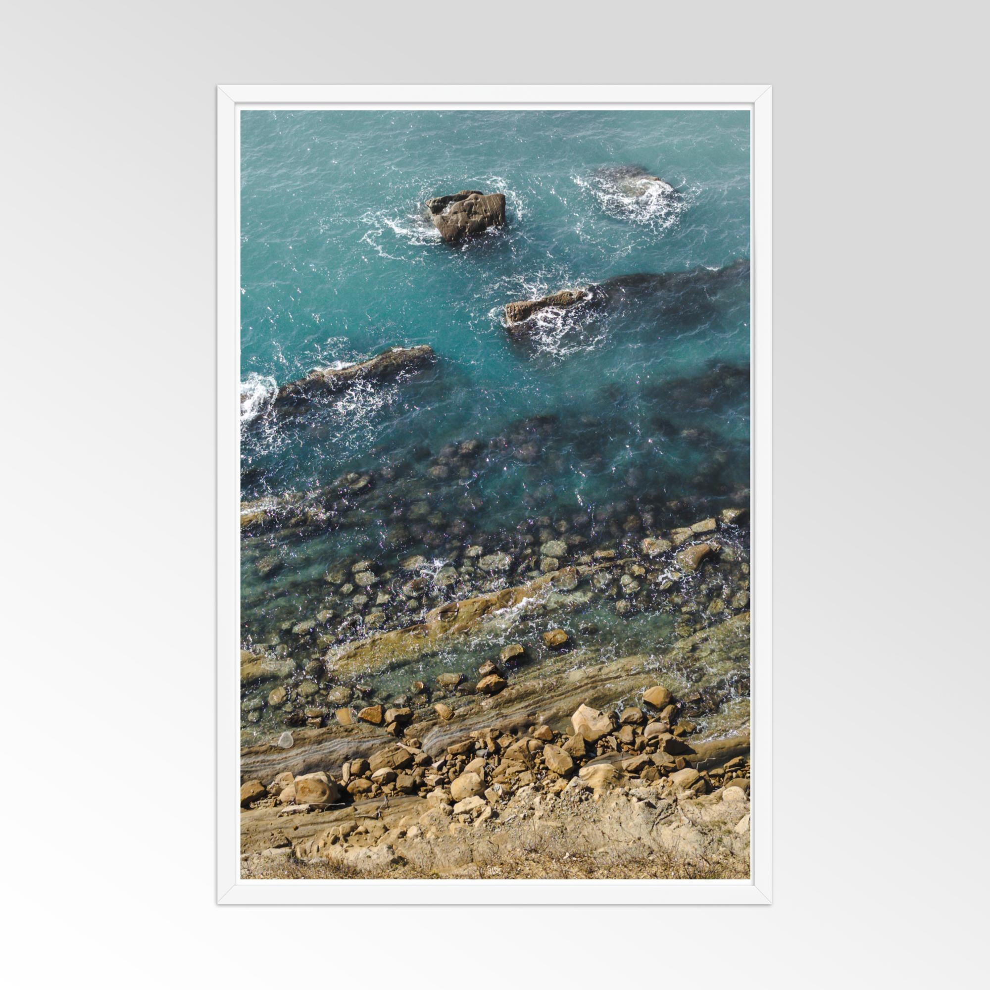 Framed artwork of a coastal scene with rocks and water.