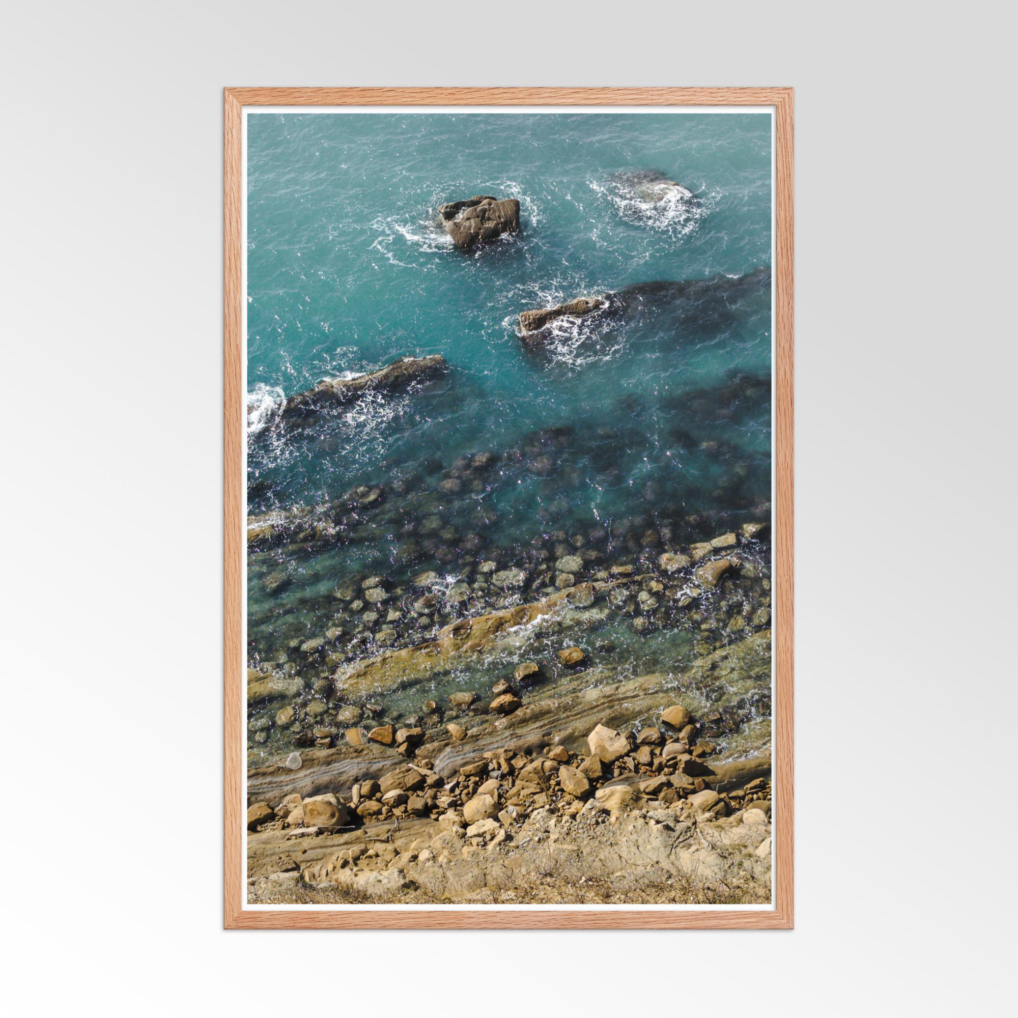 Framed artwork of a coastal scene with rocks and water.