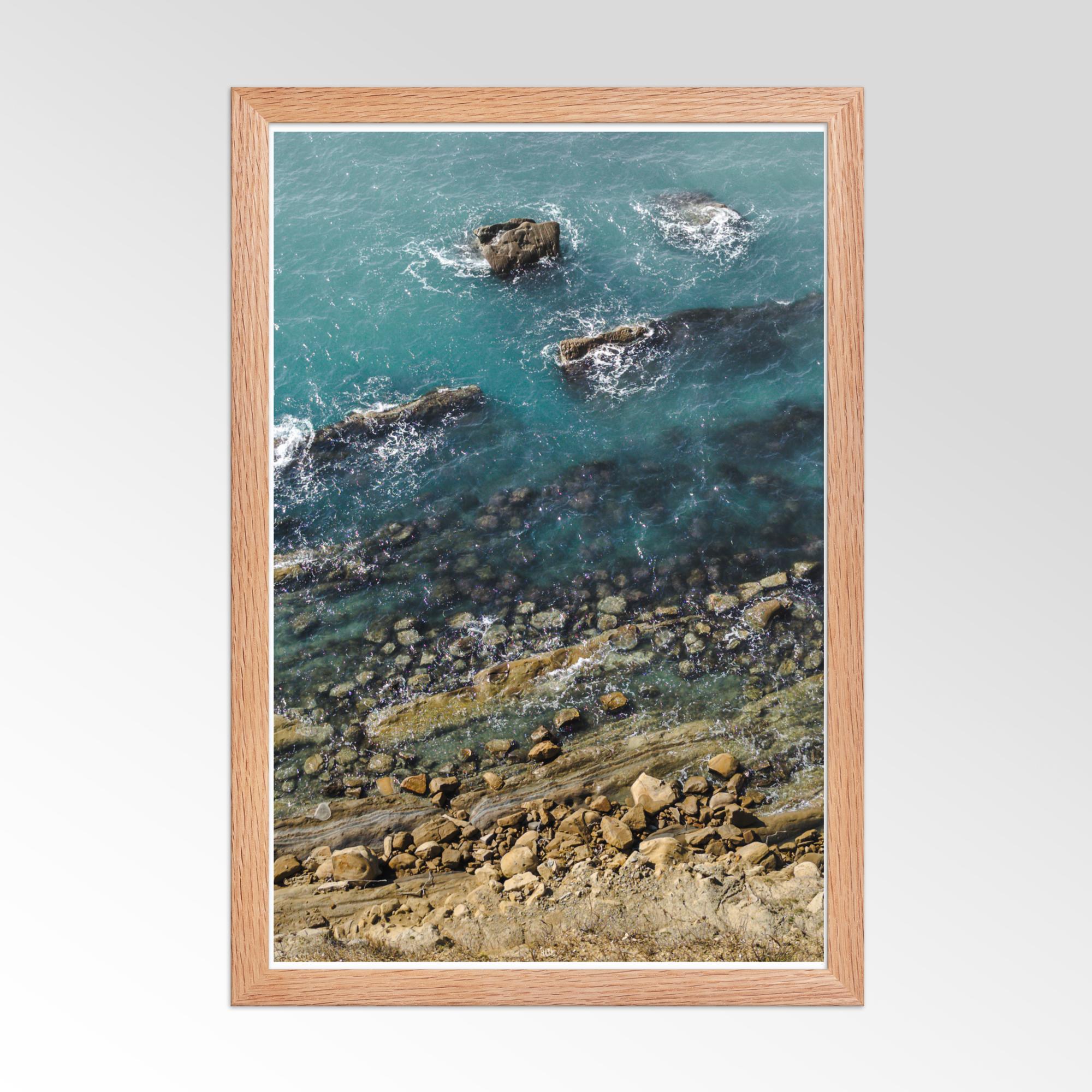 Framed artwork of a coastal scene with rocks and water.
