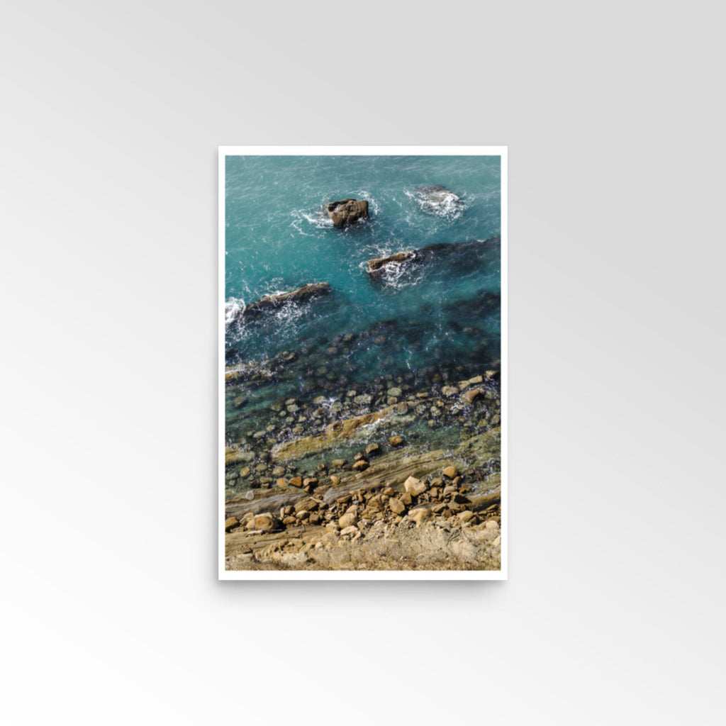Framed artwork of a coastal scene with rocks and water.