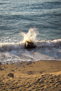 Wave crashing onto a rocky shore with sand and small rocks.