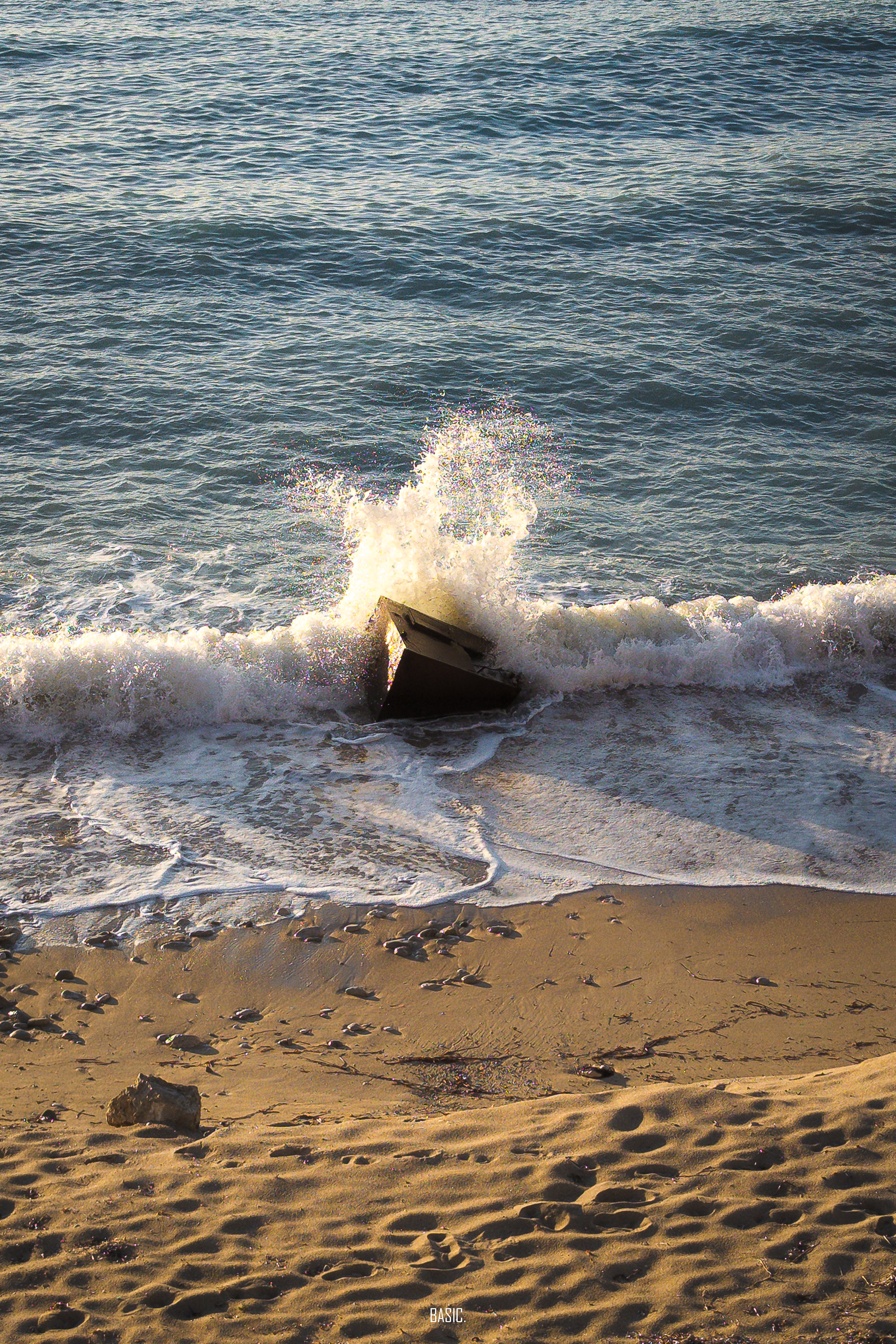 Wave crashing onto a rocky shore with sand and small rocks.