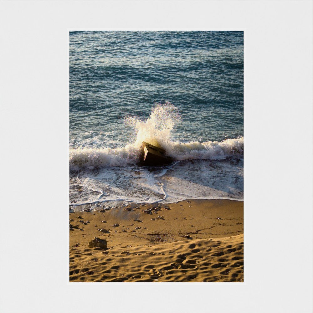 Wave crashing on a rocky beach with sand and water.