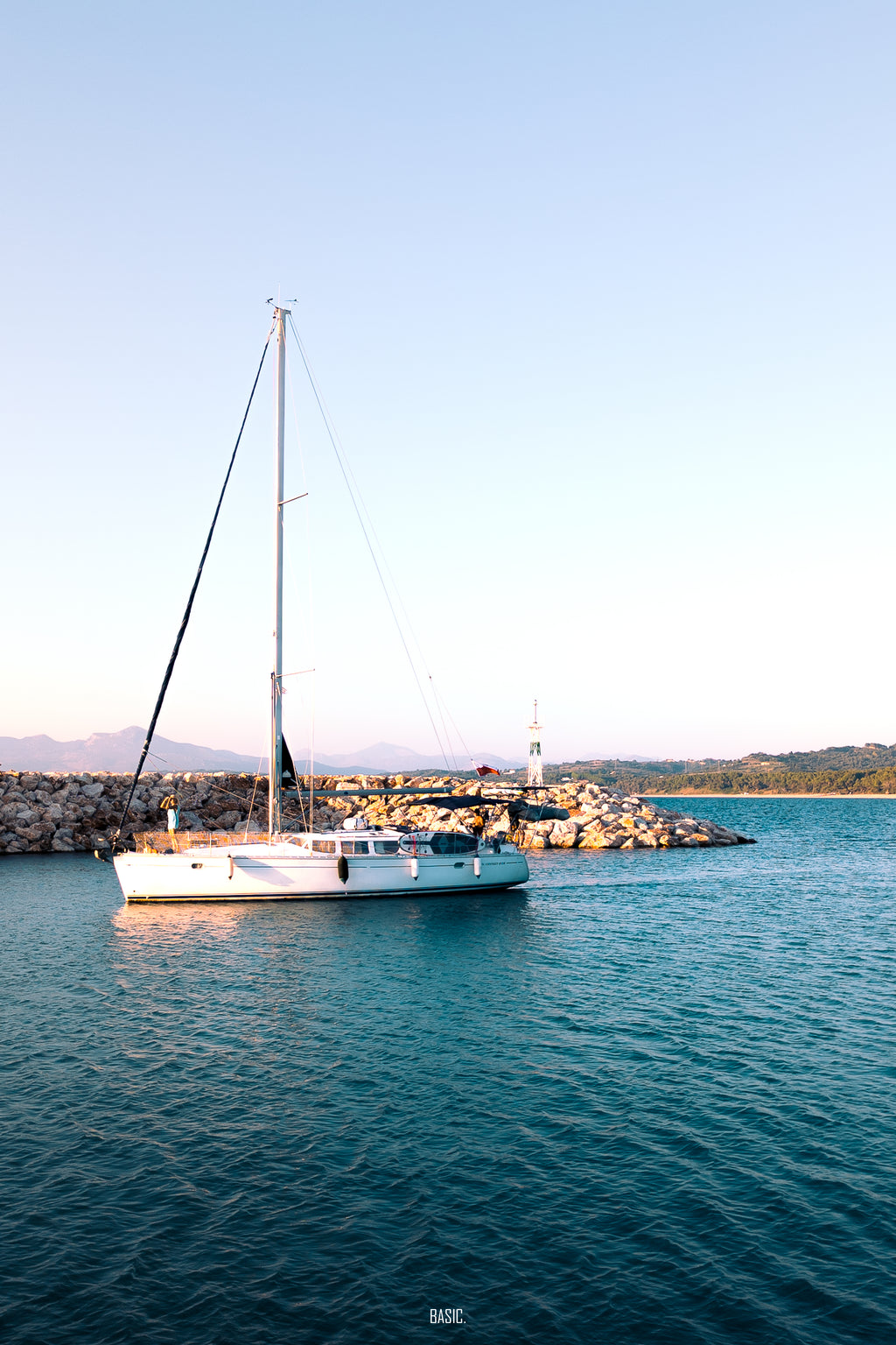 Sailboat anchored in calm water with a lighthouse in the background