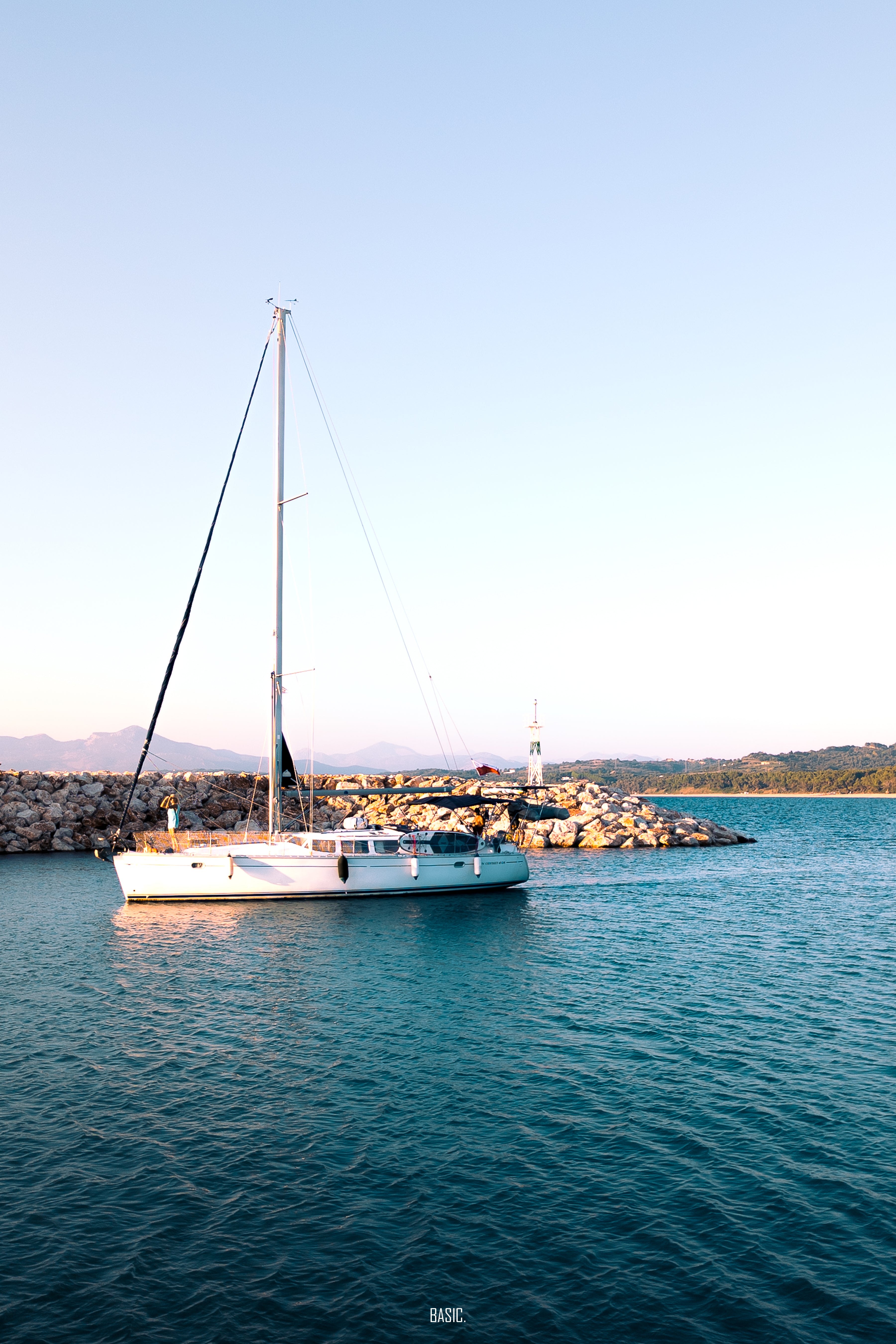 Sailboat anchored in calm water with a lighthouse in the background