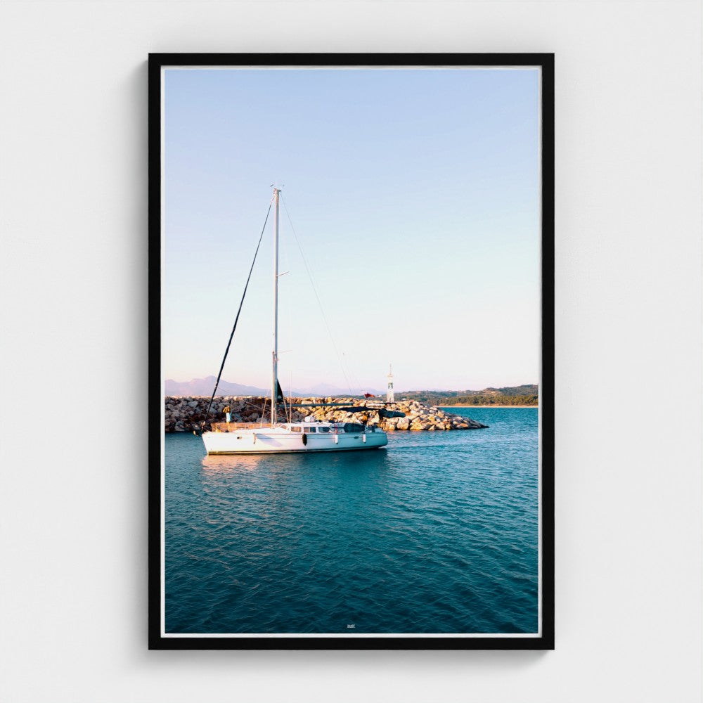 Framed photograph of a sailboat on a body of water with a cityscape in the background.